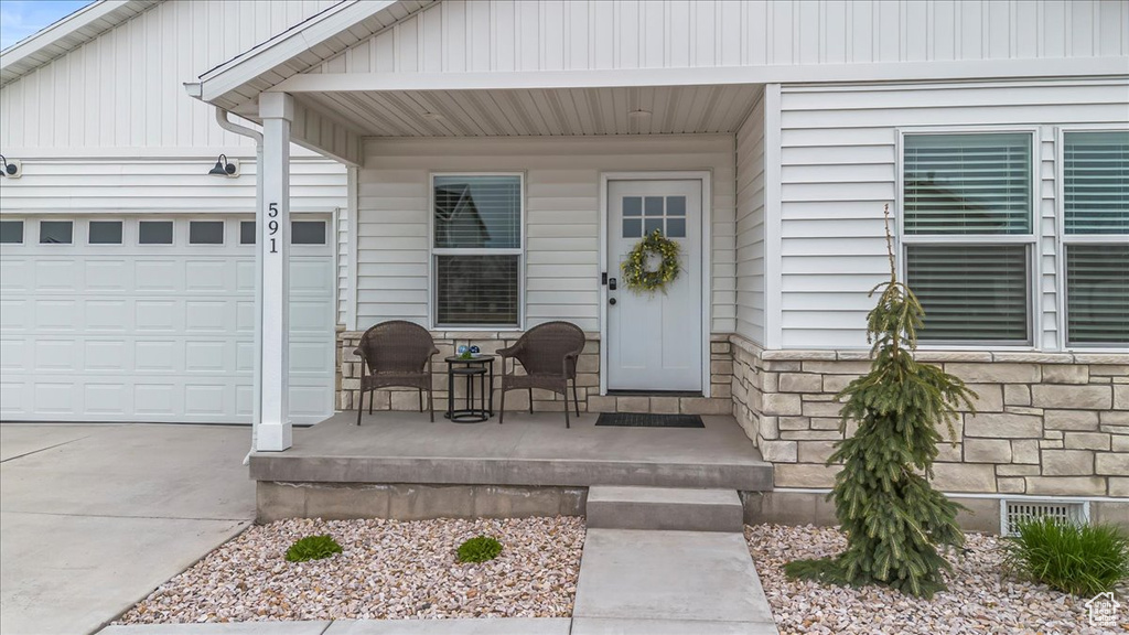 View of exterior entry featuring a porch, an attached garage, driveway, and stone siding