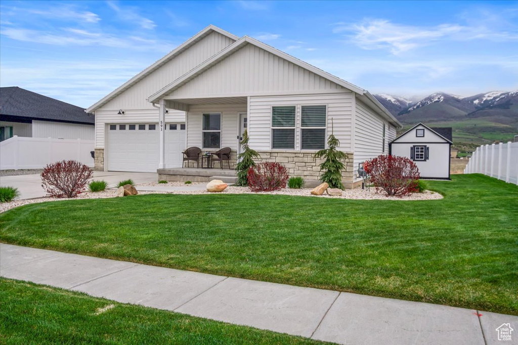 View of front of home featuring covered porch, fence, a front lawn, an attached garage, and stone siding
