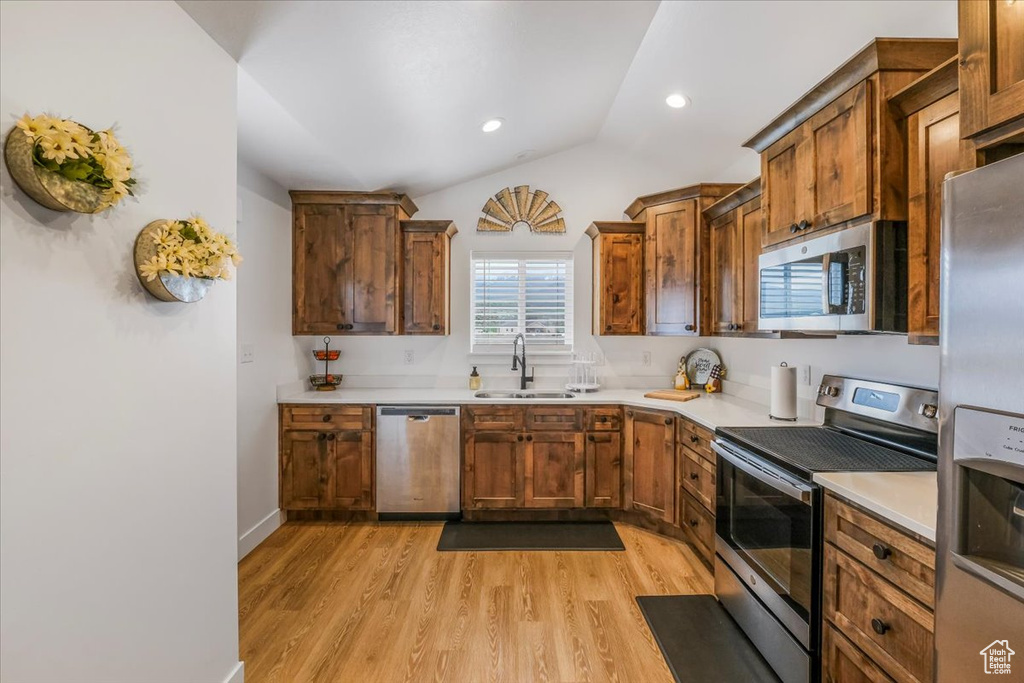 Kitchen with a sink, appliances with stainless steel finishes, vaulted ceiling, and light wood-type flooring