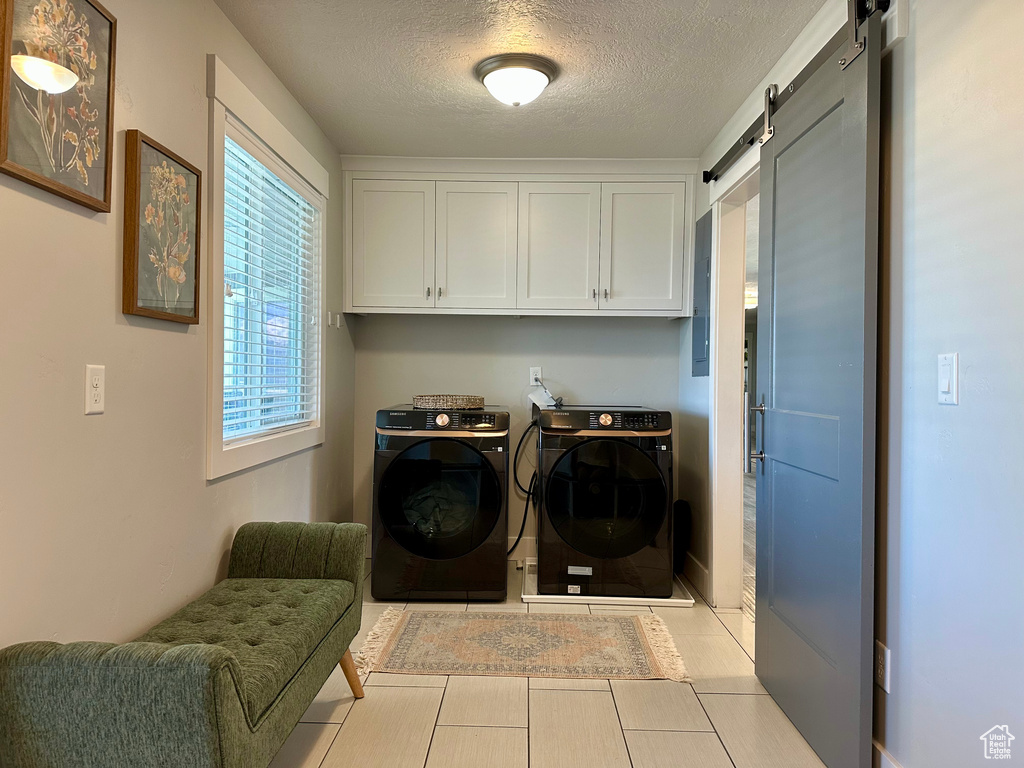 Laundry area with a textured ceiling, tile patterned flooring, washing machine and dryer, cabinet space, and a barn door
