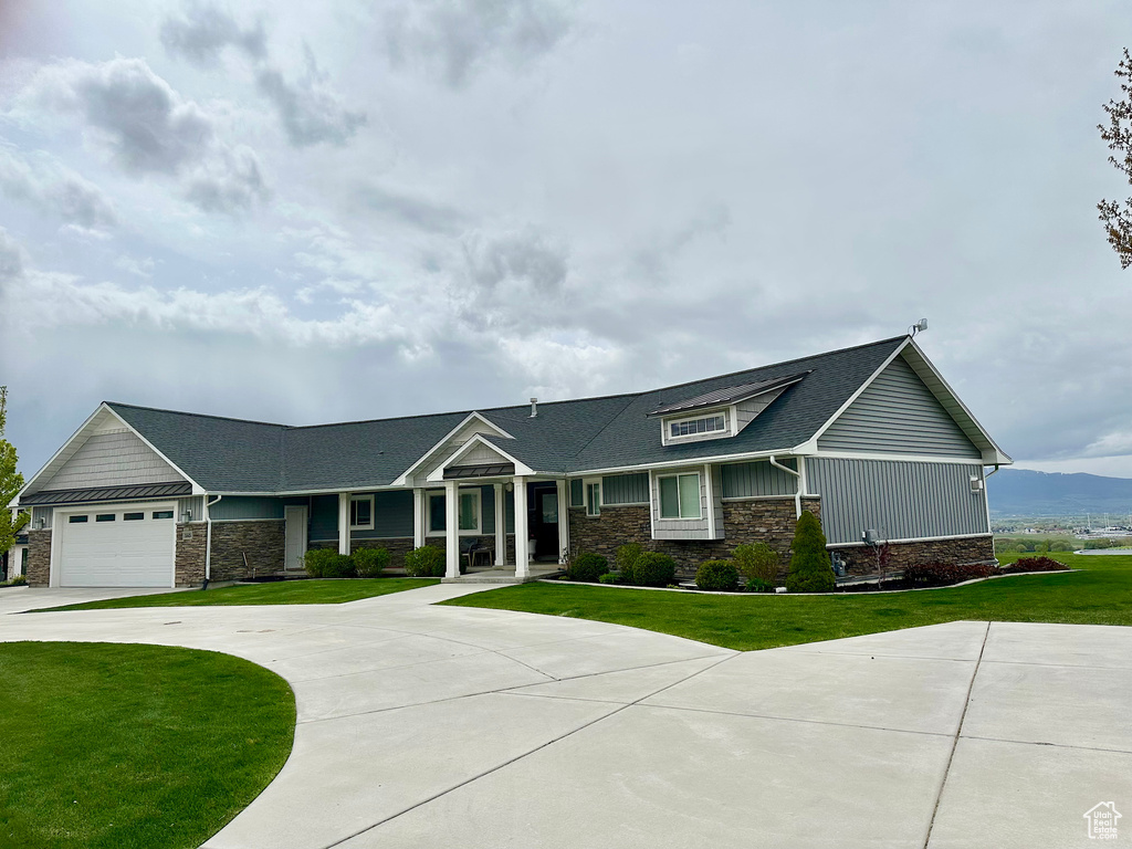 Craftsman-style home with an attached garage, concrete driveway, a front lawn, and stone siding