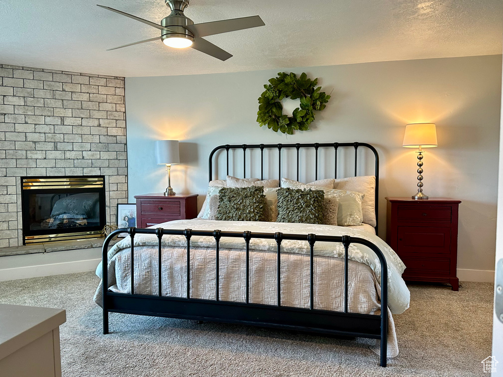 Bedroom with ceiling fan, a textured ceiling, a fireplace, carpet floors, and baseboards