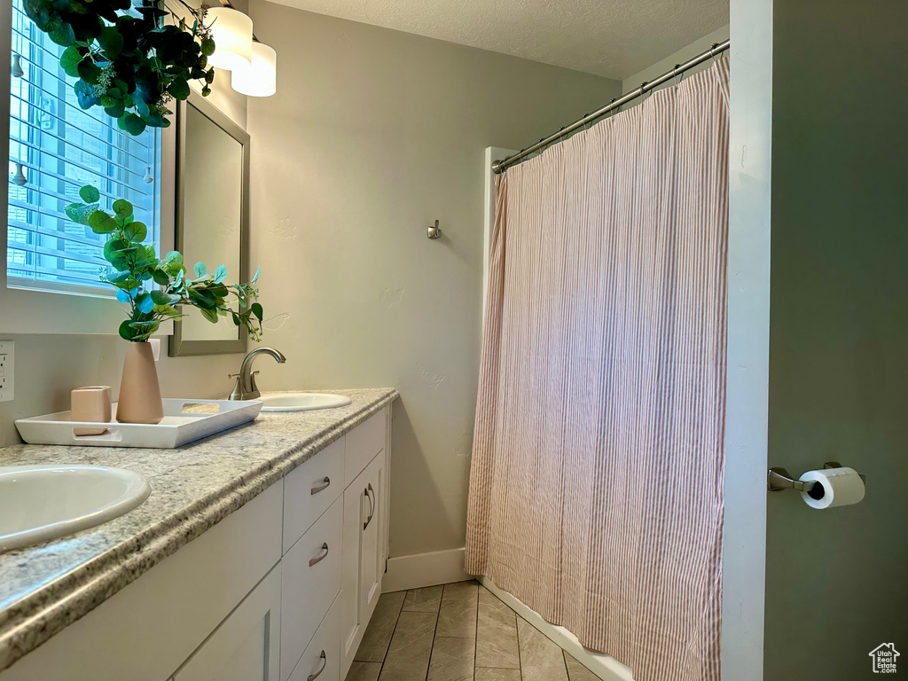 Full bathroom featuring double vanity, tile patterned floors, curtained shower, and a sink