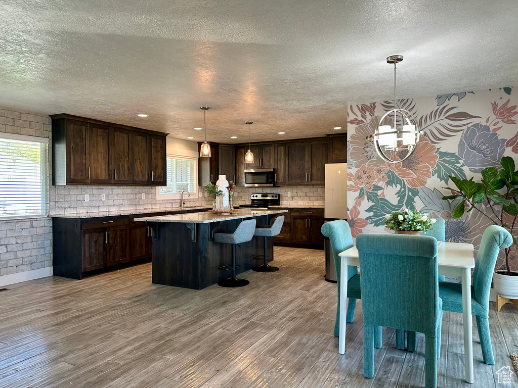 Kitchen with a kitchen island, dark brown cabinets, a textured ceiling, a sink, and appliances with stainless steel finishes