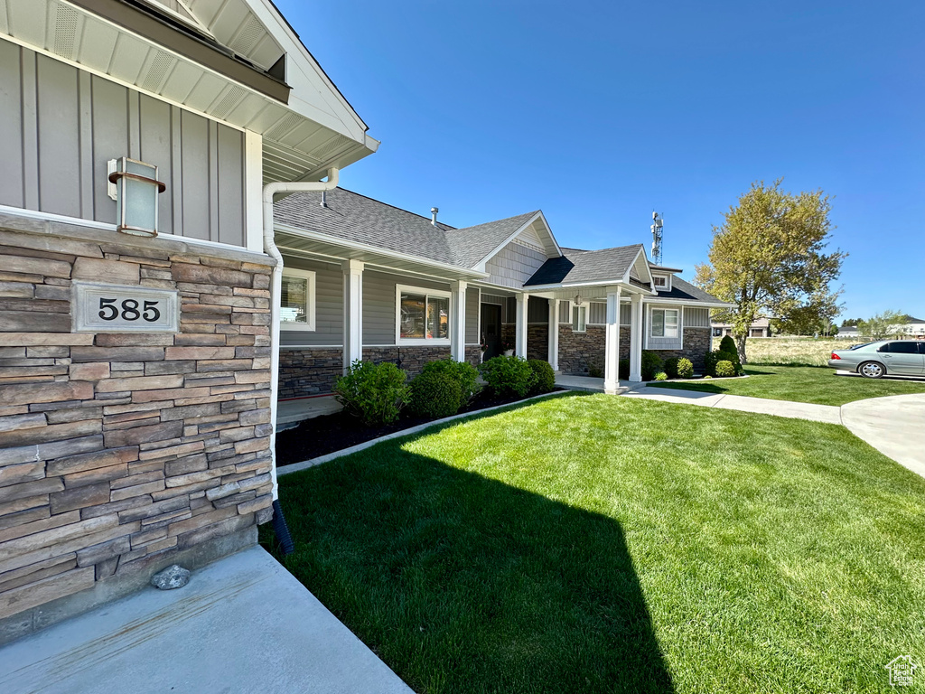 Exterior space with a shingled roof, board and batten siding, a yard, and stone siding