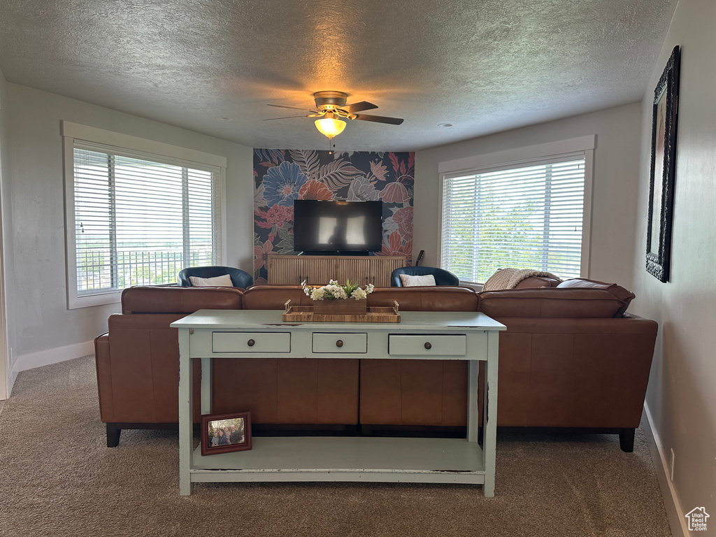 Carpeted living room featuring a textured ceiling, a ceiling fan, and baseboards