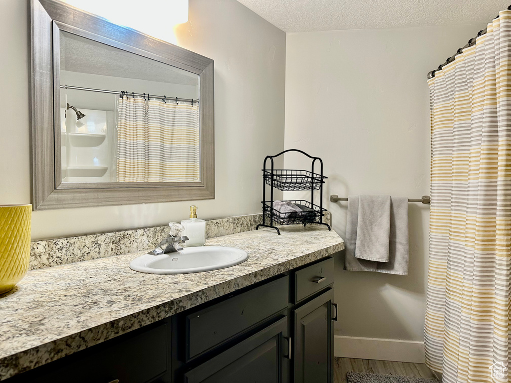 Bathroom with a shower with curtain, a textured ceiling, wood finished floors, vanity, and baseboards