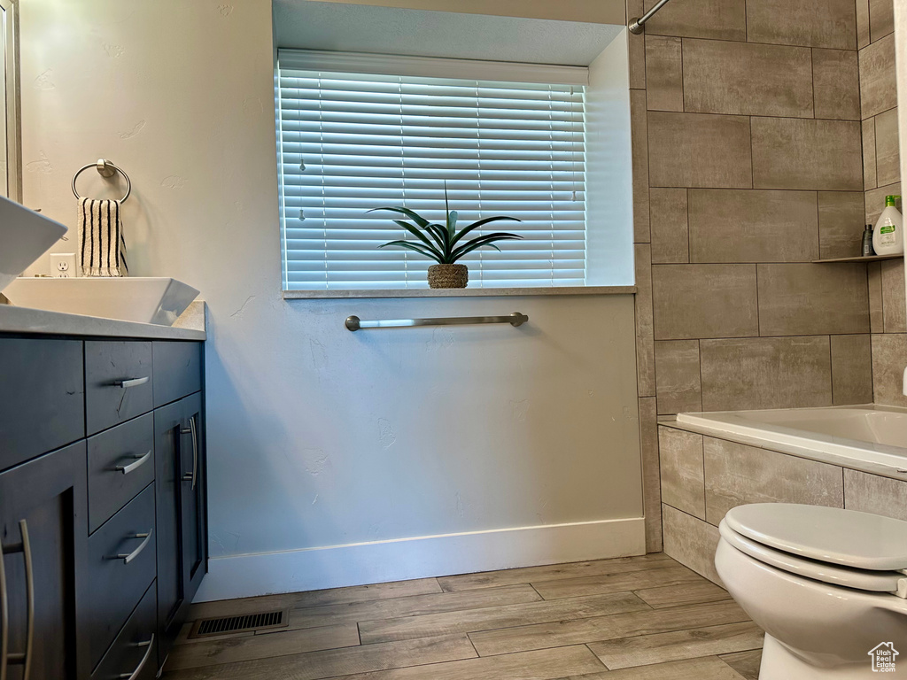 Bathroom featuring tiled tub, wood finished floors, vanity, baseboards, and toilet