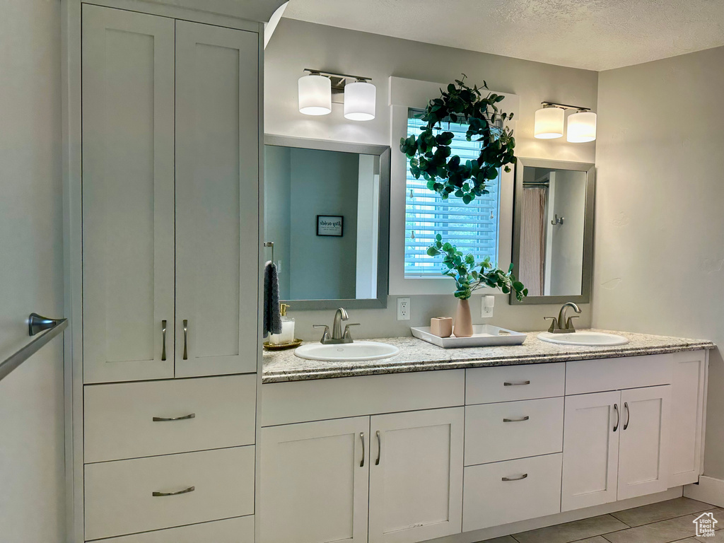 Full bath with double vanity, a sink, a textured ceiling, and tile patterned floors