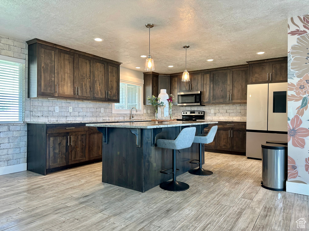 Kitchen with freestanding refrigerator, a textured ceiling, stainless steel microwave, and a kitchen bar