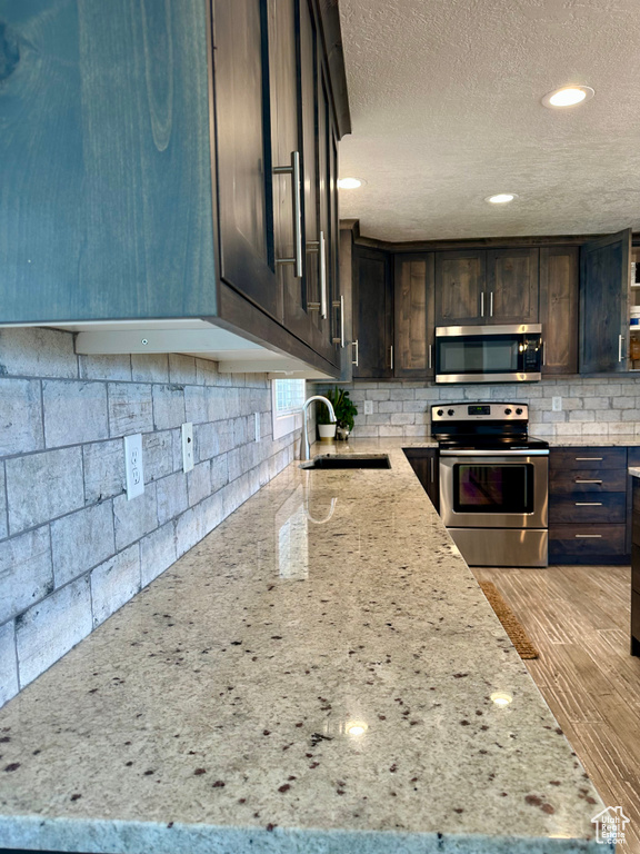 Kitchen with a sink, appliances with stainless steel finishes, dark brown cabinetry, and a textured ceiling