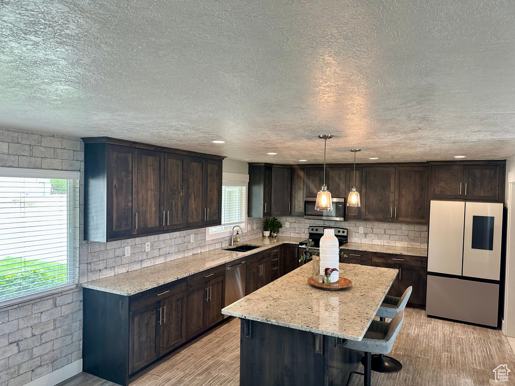 Kitchen featuring stainless steel appliances, a sink, dark brown cabinetry, a breakfast bar, and a center island