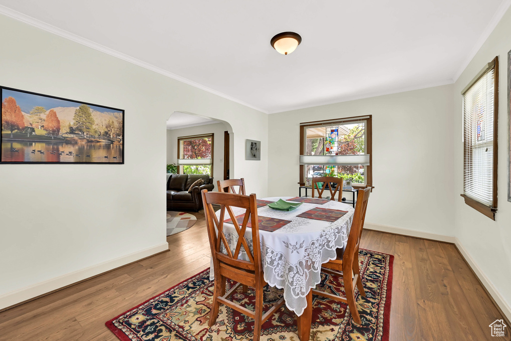 Dining room featuring baseboards, arched walkways, wood finished floors, and ornamental molding