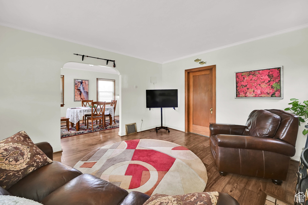 Living room featuring visible vents, crown molding, arched walkways, wood finished floors, and baseboards