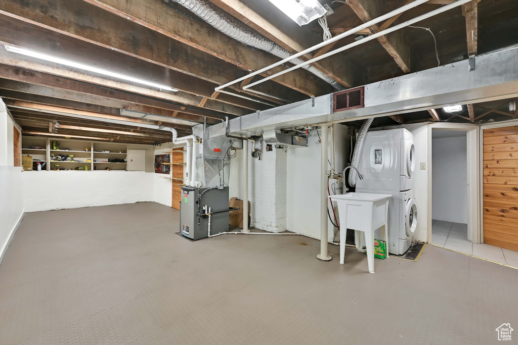 Unfinished below grade area with a sink, stacked washing maching and dryer, heating unit, and visible vents
