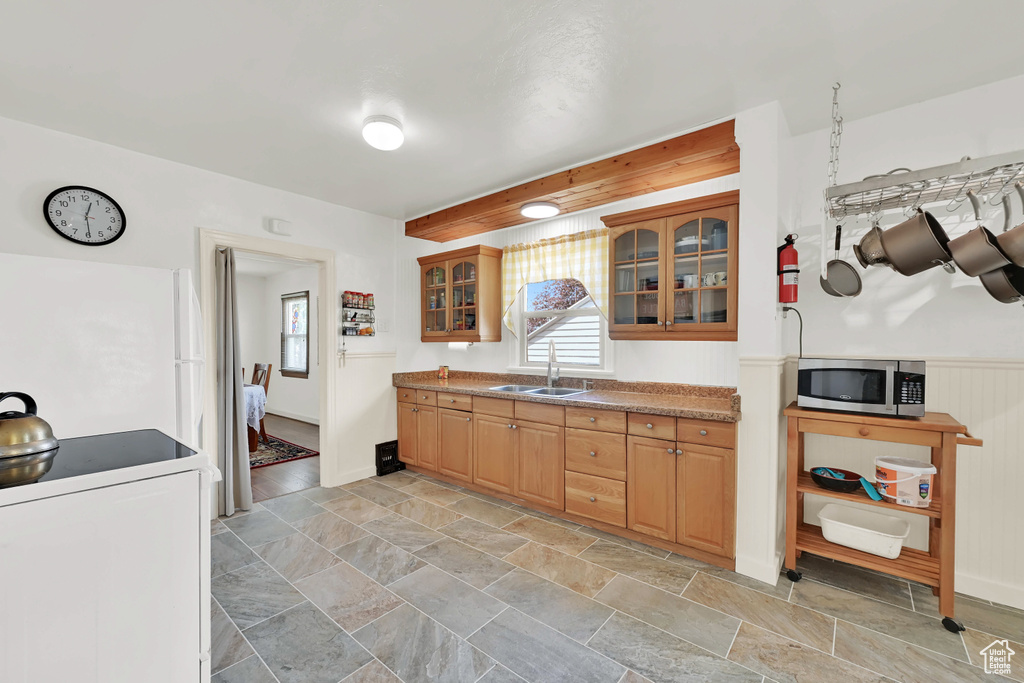 Kitchen featuring a sink, stone finish floor, stainless steel microwave, washer / dryer, and glass insert cabinets
