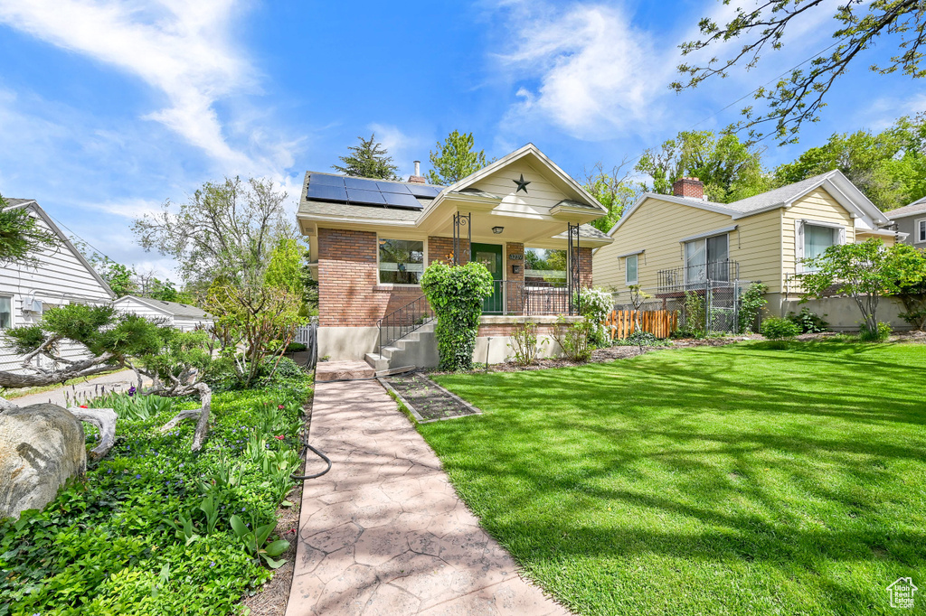 Bungalow-style house with fence, covered porch, a front yard, brick siding, and solar panels