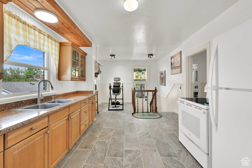 Kitchen featuring a sink, stone finish floor, white appliances, and glass insert cabinets