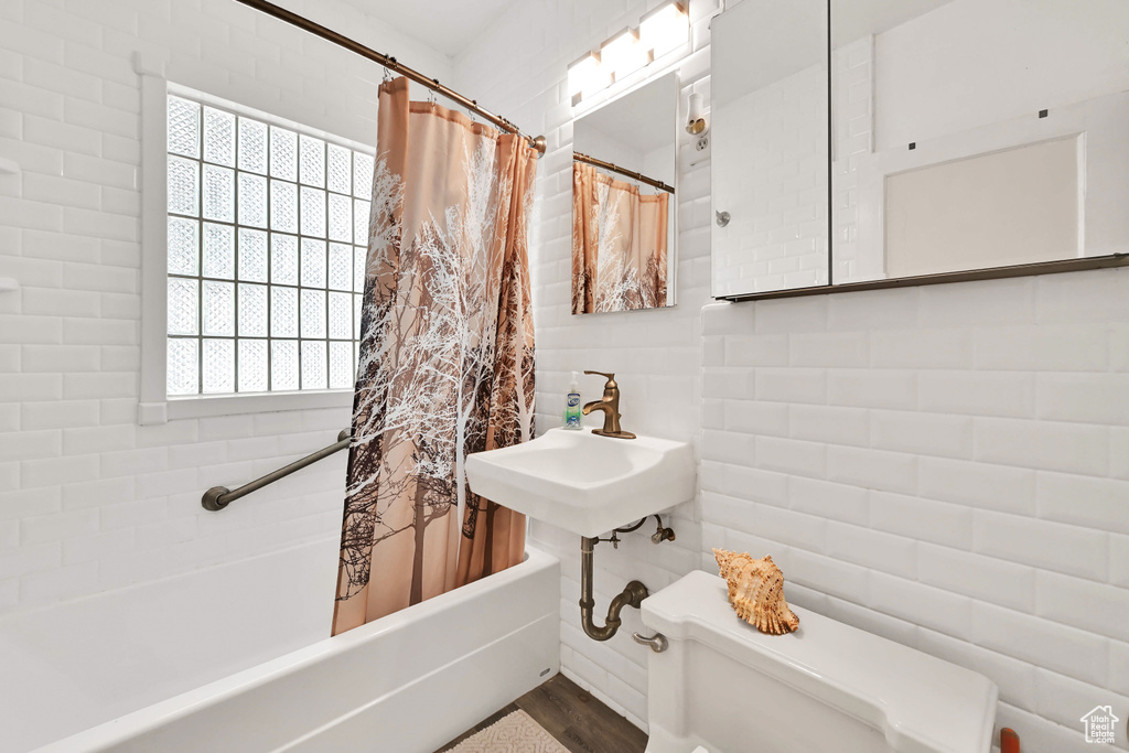 Full bathroom featuring a sink, shower / bath combo, toilet, tile walls, and wood finished floors