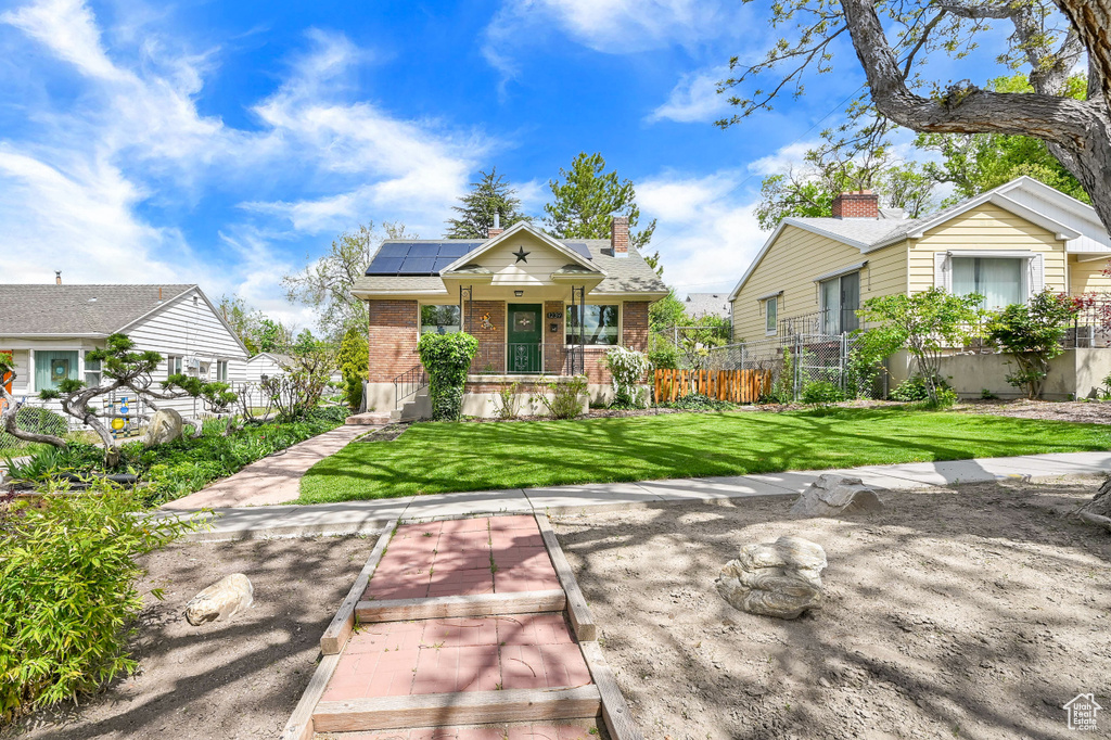 Bungalow with roof mounted solar panels, fence, a front yard, and brick siding