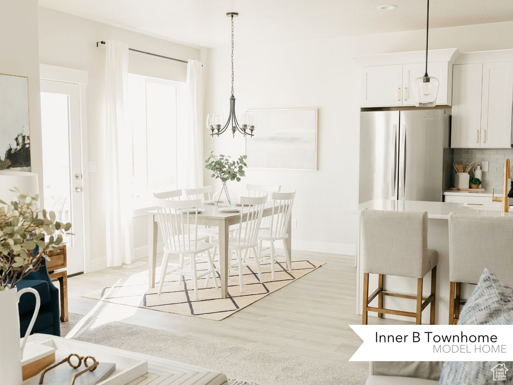 Kitchen featuring backsplash, baseboards, freestanding refrigerator, a notable chandelier, and light wood-style flooring