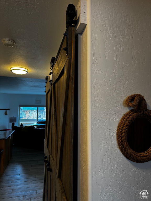 Corridor featuring a barn door, hardwood / wood-style flooring, a textured ceiling, and a textured wall