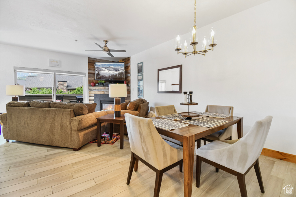 Dining area with baseboards, ceiling fan with notable chandelier, light wood finished floors, and a glass covered fireplace