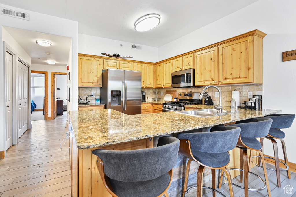 Kitchen featuring a sink, stainless steel appliances, visible vents, light stone counters, and a peninsula
