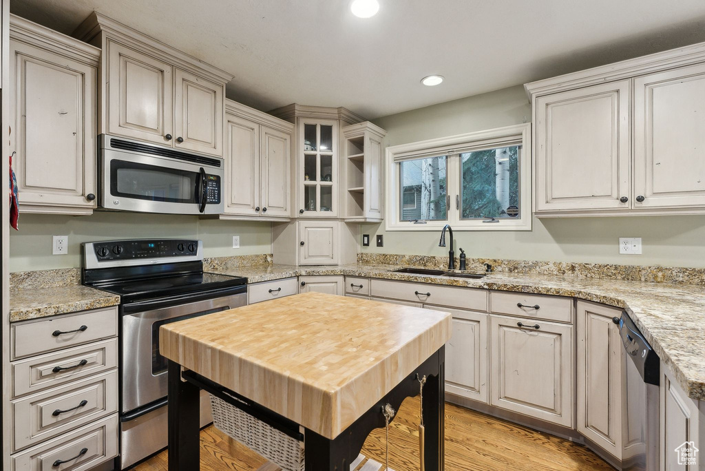 Kitchen with appliances with stainless steel finishes, a sink, light wood finished floors, recessed lighting, and glass insert cabinets