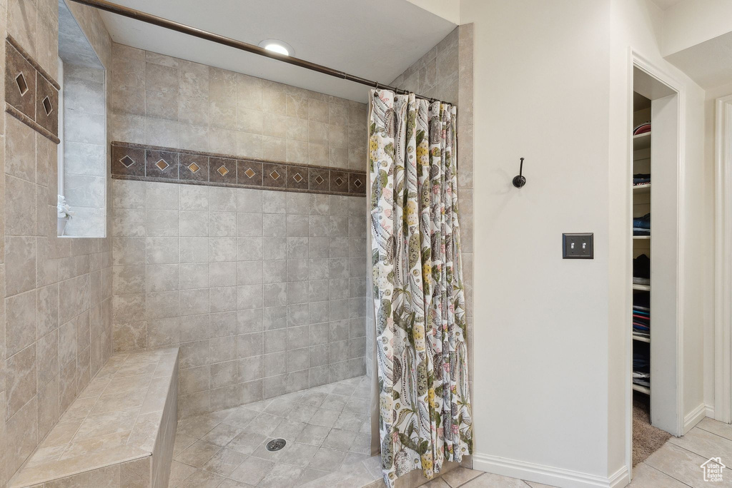 Full bath featuring baseboards, a walk in closet, tiled shower, and tile patterned floors