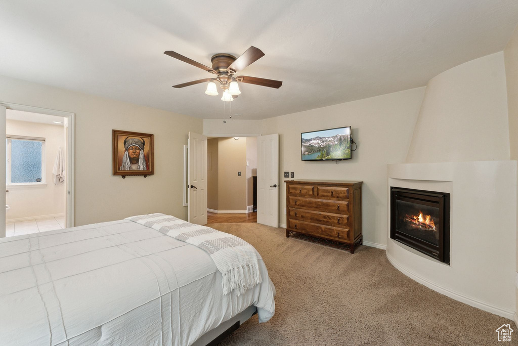 Bedroom featuring a ceiling fan, a large fireplace, baseboards, ensuite bathroom, and light carpet