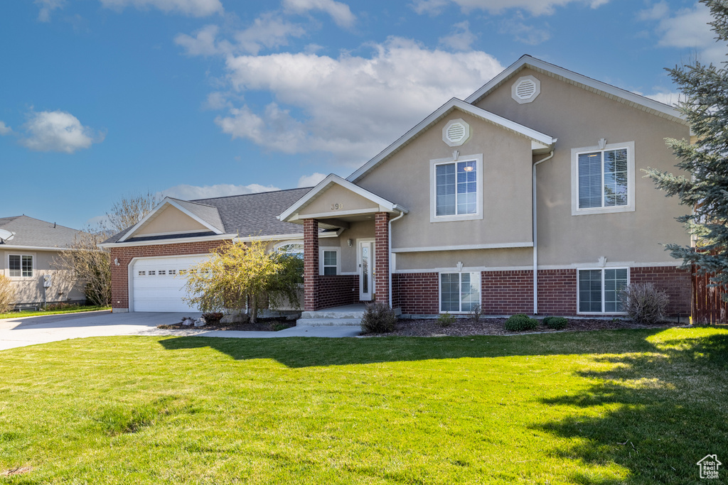 Tri-level home with stucco siding, a front yard, driveway, and brick siding