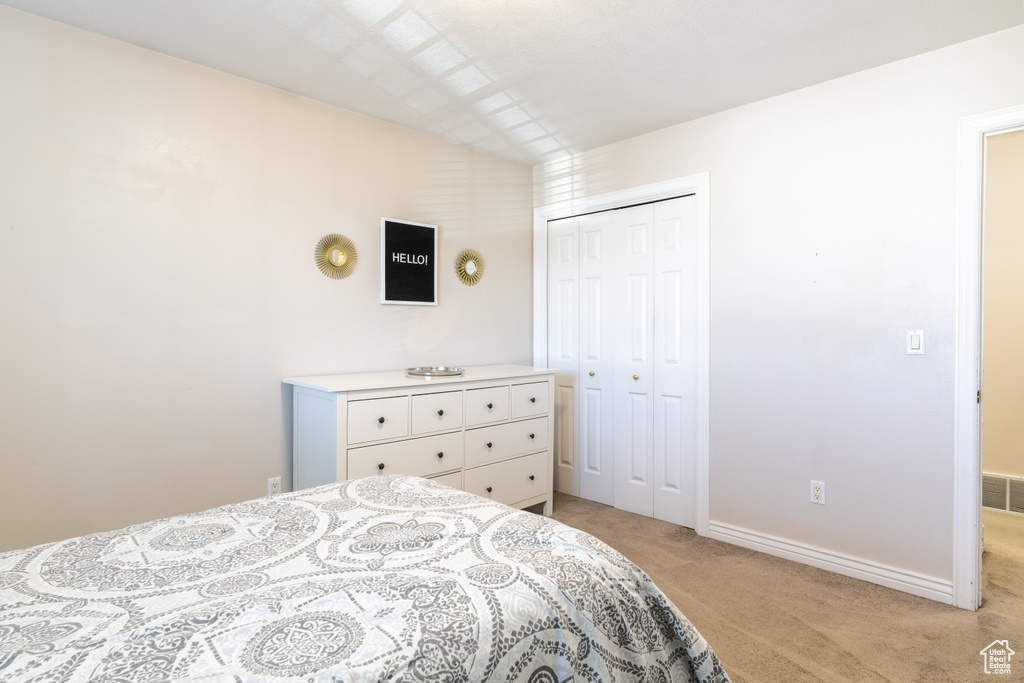 Bedroom featuring light colored carpet, baseboards, visible vents, and a closet