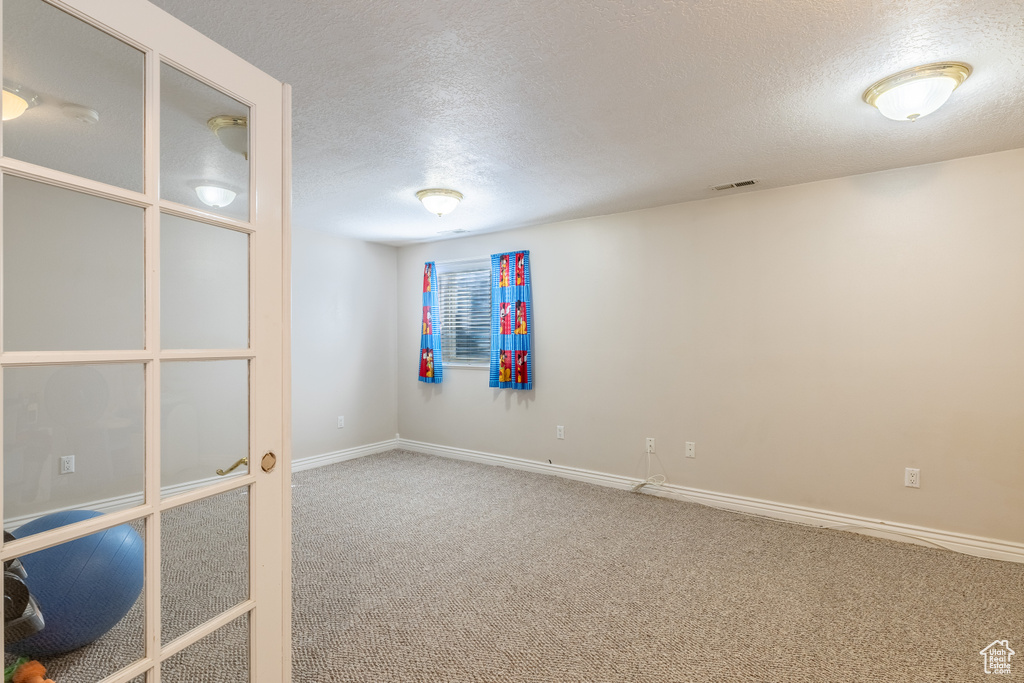 Empty room with visible vents, carpet, a textured ceiling, and baseboards