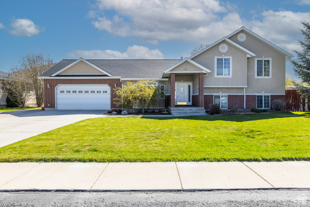 Tri-level home with an attached garage, driveway, a front lawn, and brick siding