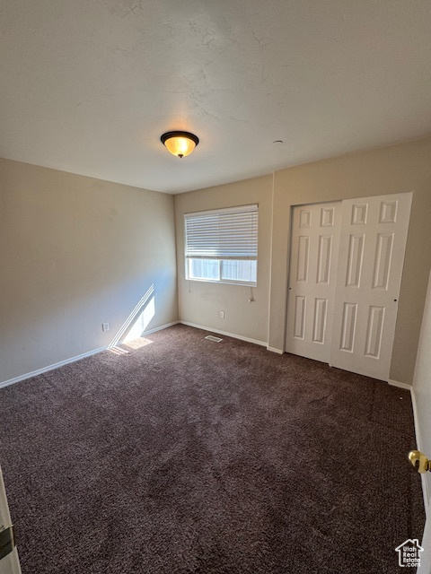 Unfurnished bedroom with baseboards, a closet, dark colored carpet, and visible vents
