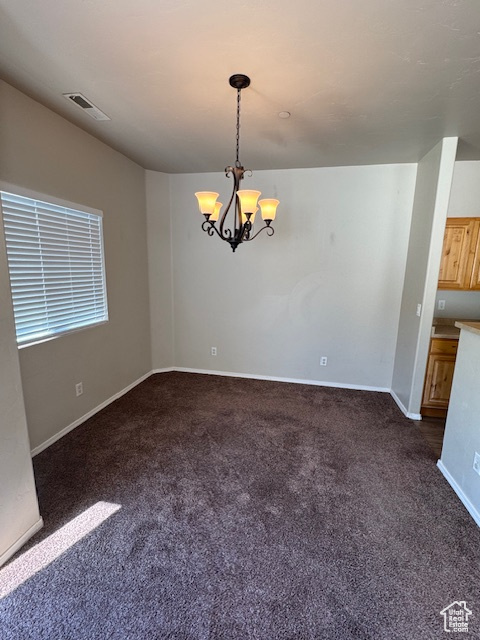 Empty room featuring dark colored carpet, baseboards, visible vents, and an inviting chandelier