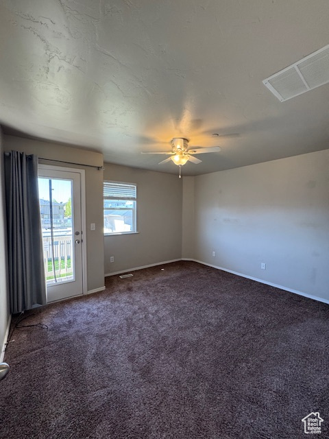 Unfurnished room featuring baseboards, a ceiling fan, dark carpet, and visible vents