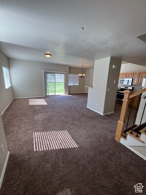 Unfurnished living room with an inviting chandelier, baseboards, and dark colored carpet