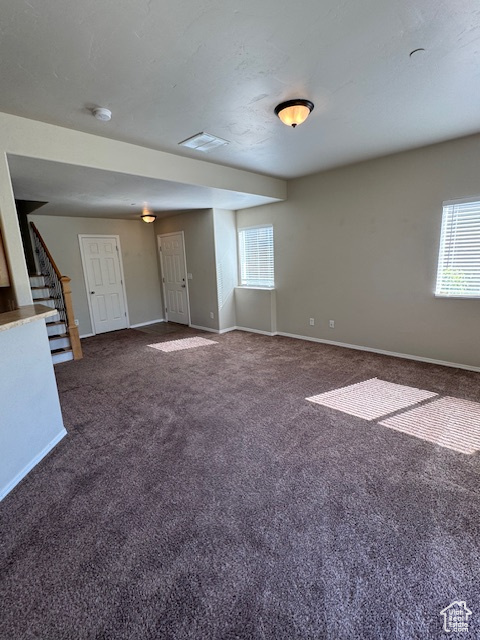 Unfurnished living room with carpet flooring, baseboards, and a healthy amount of sunlight