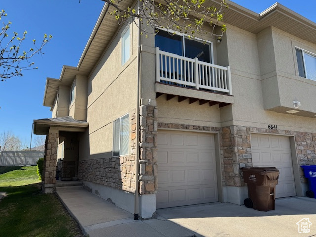 View of property exterior with a balcony, stucco siding, an attached garage, and stone siding