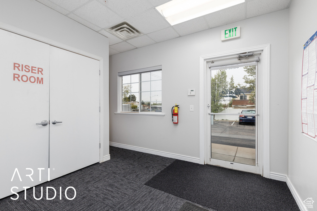 Interior space featuring dark colored carpet, baseboards, a drop ceiling, and visible vents