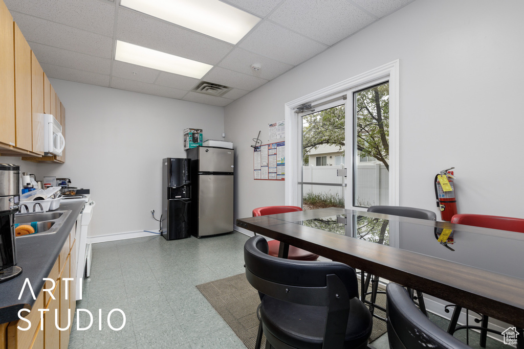 Kitchen with white microwave, a paneled ceiling, freestanding refrigerator, light floors, and visible vents