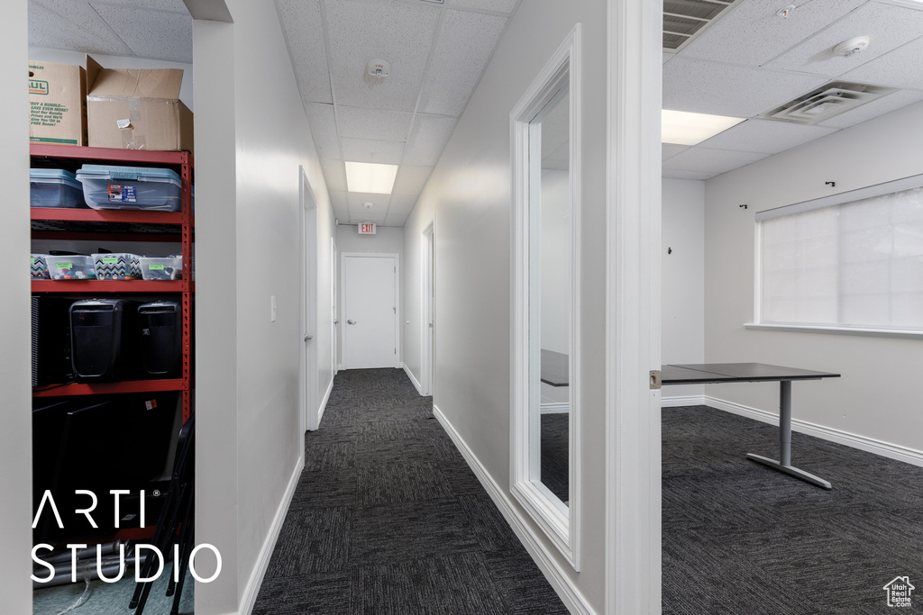 Hall featuring dark carpet, baseboards, a drop ceiling, and visible vents
