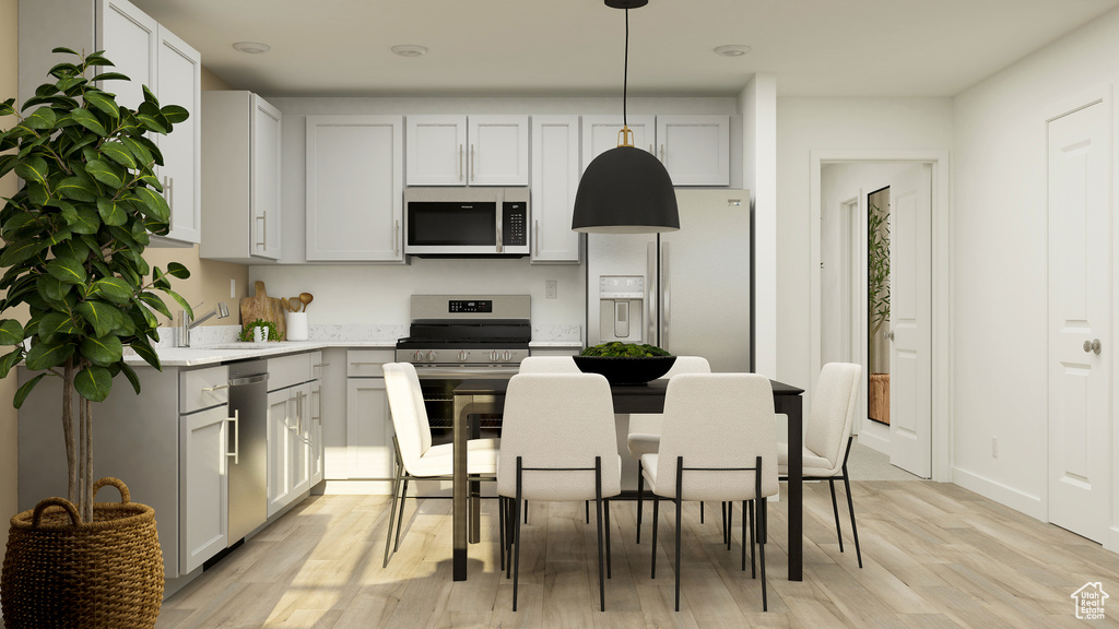 Kitchen featuring appliances with stainless steel finishes, a sink, light countertops, light wood-type flooring, and pendant lighting