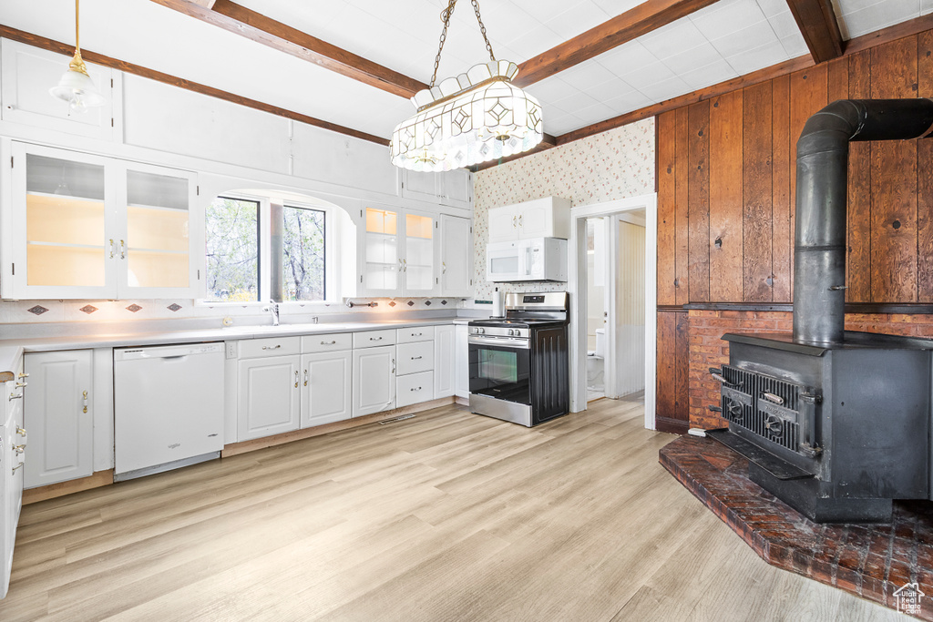 Kitchen featuring a wood stove, white appliances, beamed ceiling, light countertops, and white cabinets