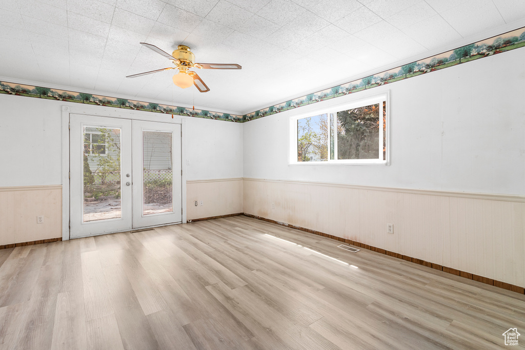 Unfurnished room with wood finished floors, ceiling fan, a wainscoted wall, and french doors