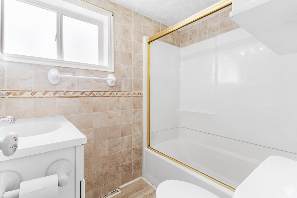 Bathroom with vanity, toilet, tile walls, combined bath / shower with glass door, and visible vents