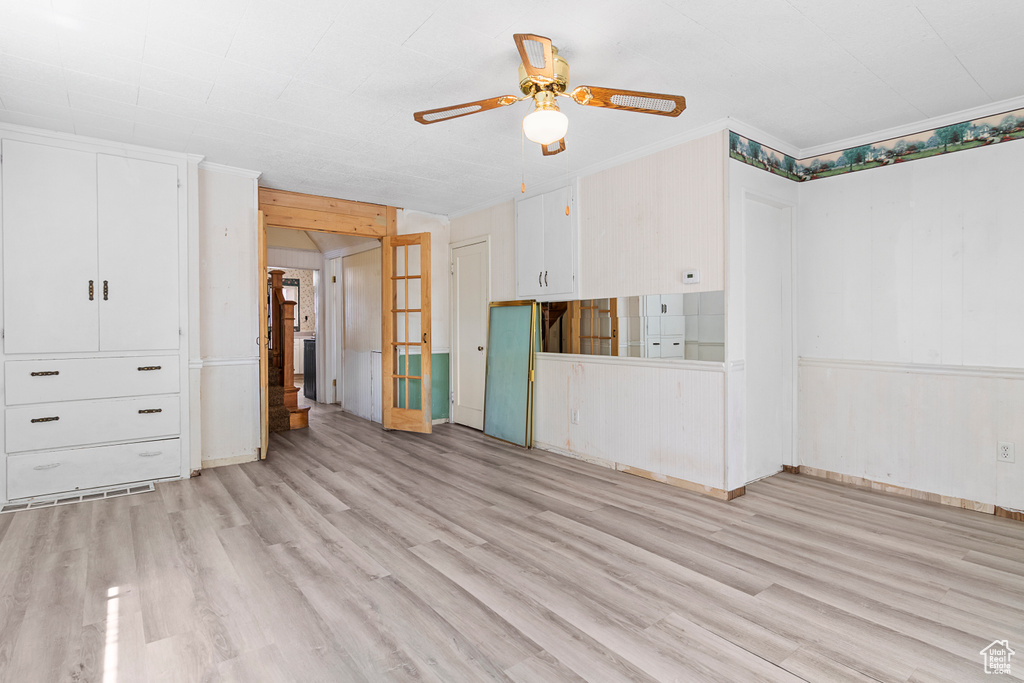 Unfurnished living room with ornamental molding, light wood-style flooring, ceiling fan, and stairs