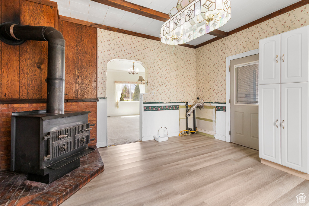 Interior space with a wood stove, beam ceiling, a wainscoted wall, light wood-style floors, and wallpapered walls